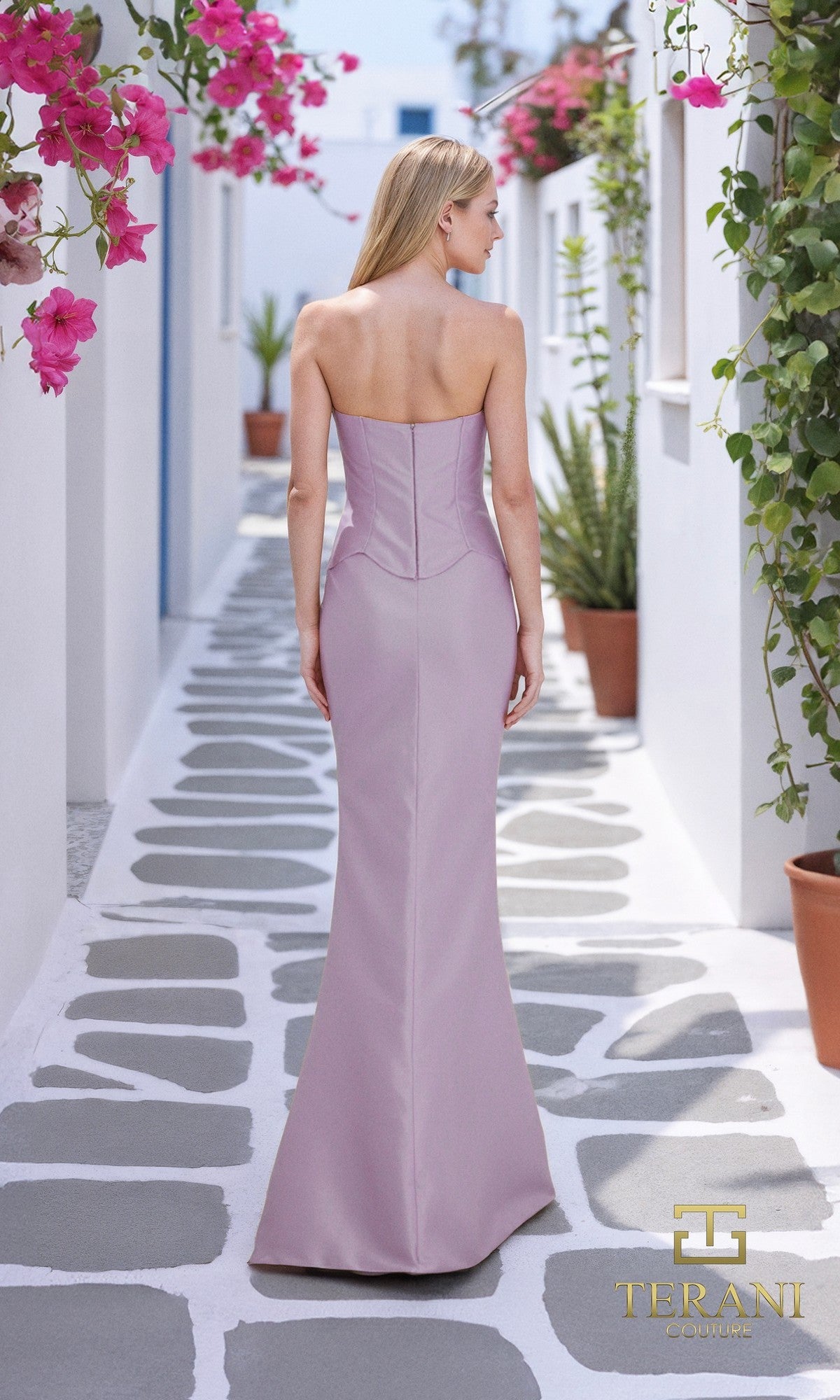 A woman wears the Terani 261E6292 long formal dress with a sheath silhouette, standing on a stone walkway with potted plants and pink flowers outdoors. The Terani Couture logo is visible in the corner.